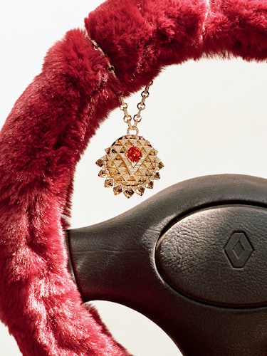 a bejeweled pendant necklace hanging from a fur-covered steering wheel