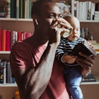 A man drinking coffee while holding his baby.