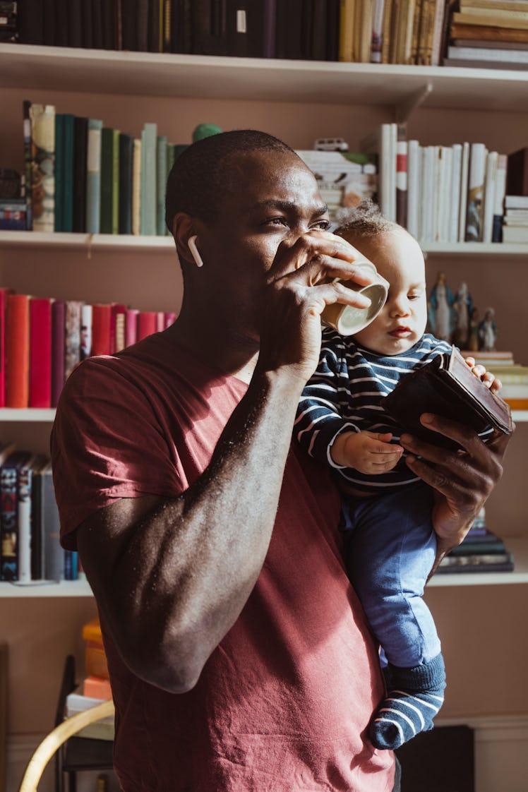 A man drinking coffee while holding his baby.