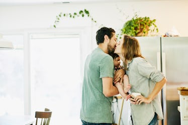 Husband and wife kissing while toddler daughter is held between them