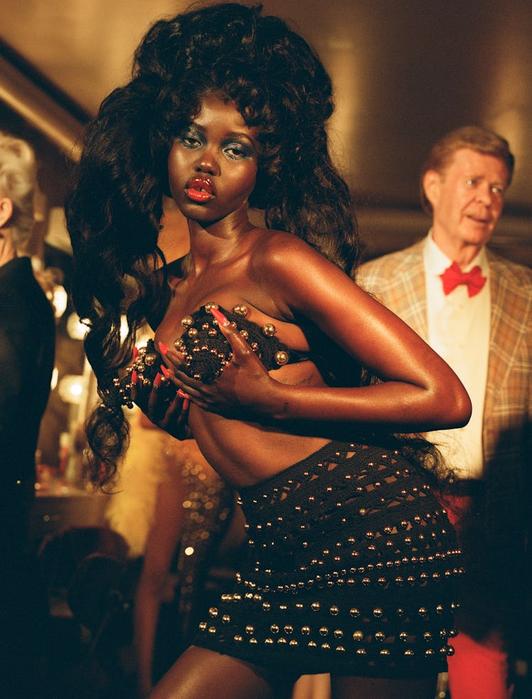 Akech wears a Schiaparelli bra top and skirt. Richard Sather wears a jacket and pants from Western C...