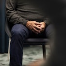 一位老人坐在椅子上，双手放在腹股沟前面。