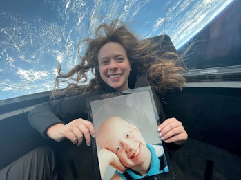 color photo of a woman floating weightless, holding a picture of a child, with earth in the backgrou...