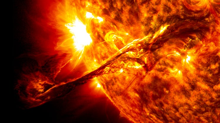 Color image of a plume of plasma bursting outward from the surface of the Sun, in oranges and yellow...