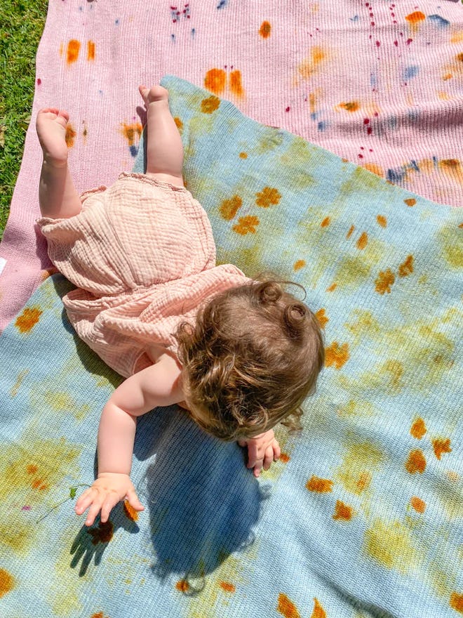 A baby crawls across two pink and blue blankets with natural tie dye patterns