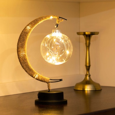 Crescent moon lamp wrapped in twine with a glass ornament hanging from it filled with twinkle lights