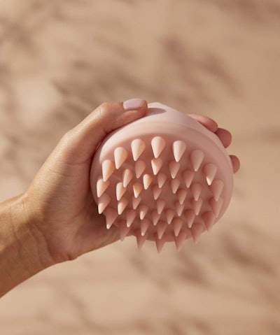 Hand holding up a blush pink silicone scalp massager