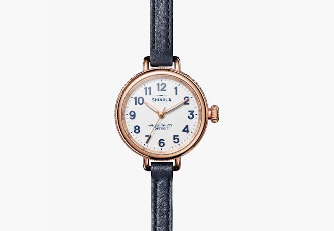 A gold women's watch with thin, black leather wrist strap