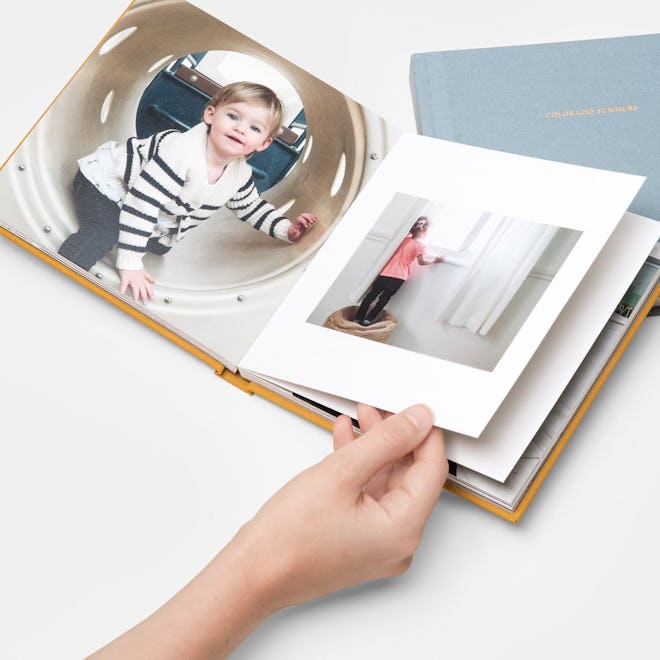A hand flips through a photo book with children's pictures printed inside