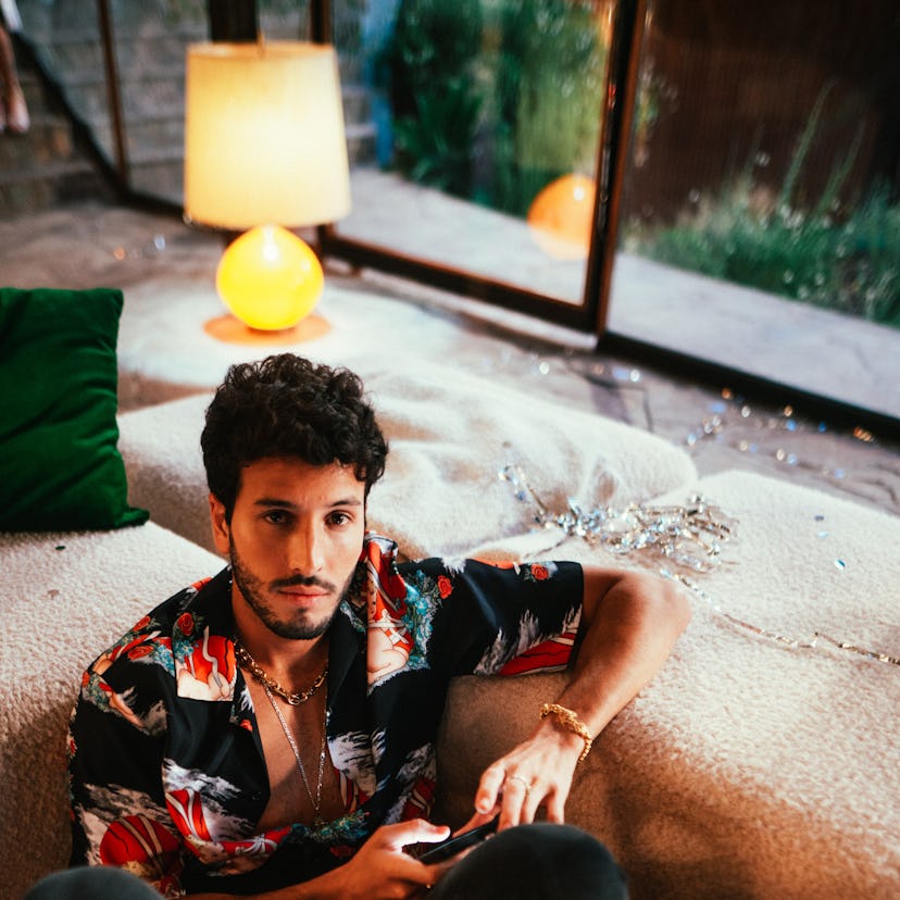 Sebastián Yatra sitting on the floor in a colorful button down shirt