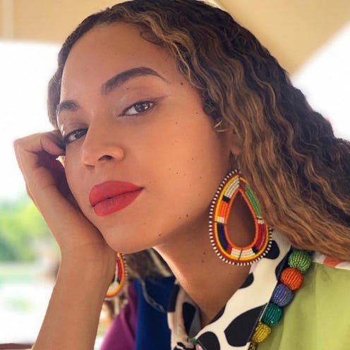 Beyonce posing with her had on her cheek with a no makeup glam with just a red lip and nothing else