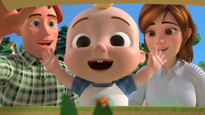 A baby smiles, his parents standing behind him.