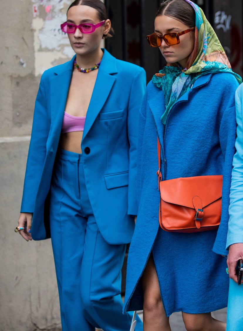 Two people wearing bright, cobalt blue outfits with pink and orange accessories at Paris Fashion Wee...