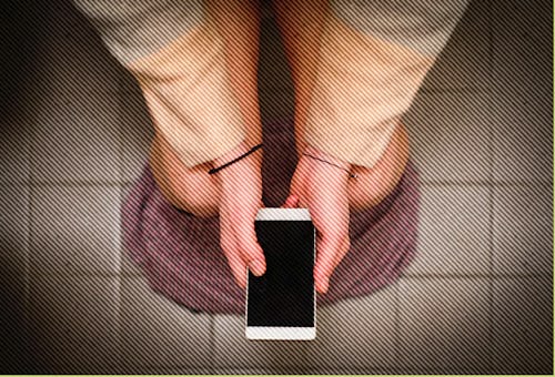 A person sitting on a toilet bowl and holding a smartphone before Super Bowl Sunday