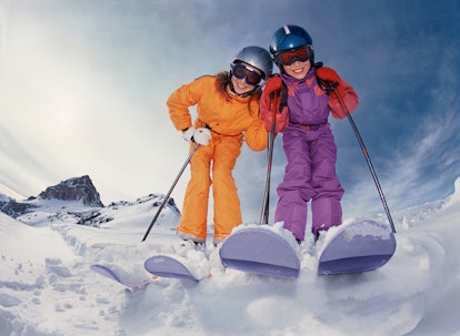 Two kids skiing in helmets smile at the camera.