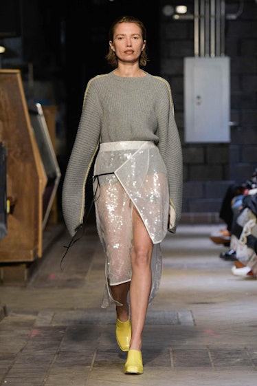 Model on the NY Fashion Week Fall 2022 runway in Eckhaus Latta grey sweater, a white skirt and yello...