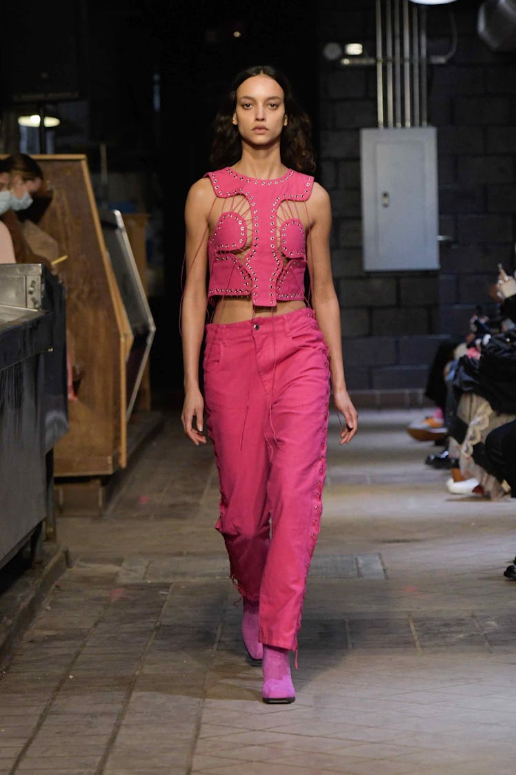 Model on the NY Fashion Week Fall 2022 runway in Eckhaus Latta pink west, pants, and heels.