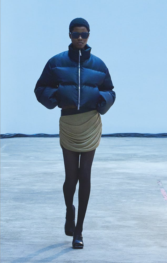 A model walking the Khaite Fall/Winter 2022 show in a short black jacket over a beige ruffled dress.