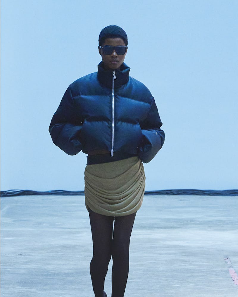 A model walking the Khaite Fall/Winter 2022 show in a short black jacket over a beige ruffled dress.