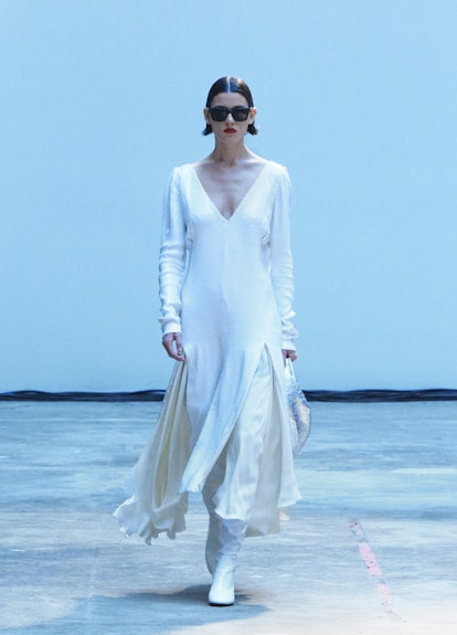 A model walking the runway in a white long-sleeved dress over white silk pants and boots during Khai...