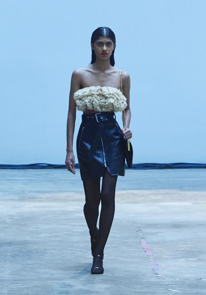 A model wearing a frilled beige top with a black belted mini leather skirt for the Khaite's fashion ...