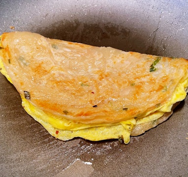 Scallion pancake with egg folded inside, on a pan.