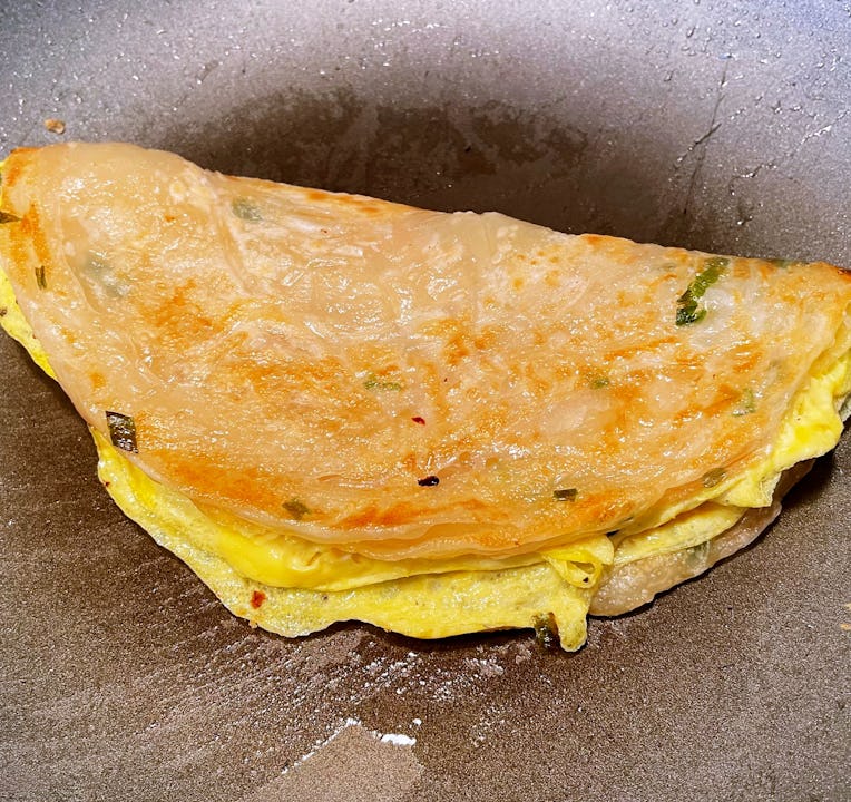 Scallion pancake with egg folded inside, on a pan.
