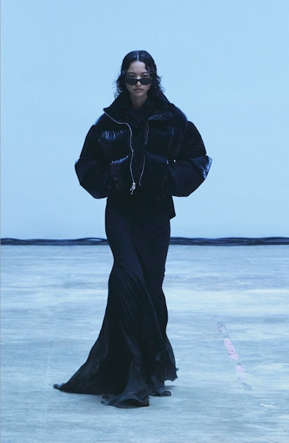 A model wearing a short black puffy jacket over a long black dress from Khaite's Fall/Winter 2022 Co...