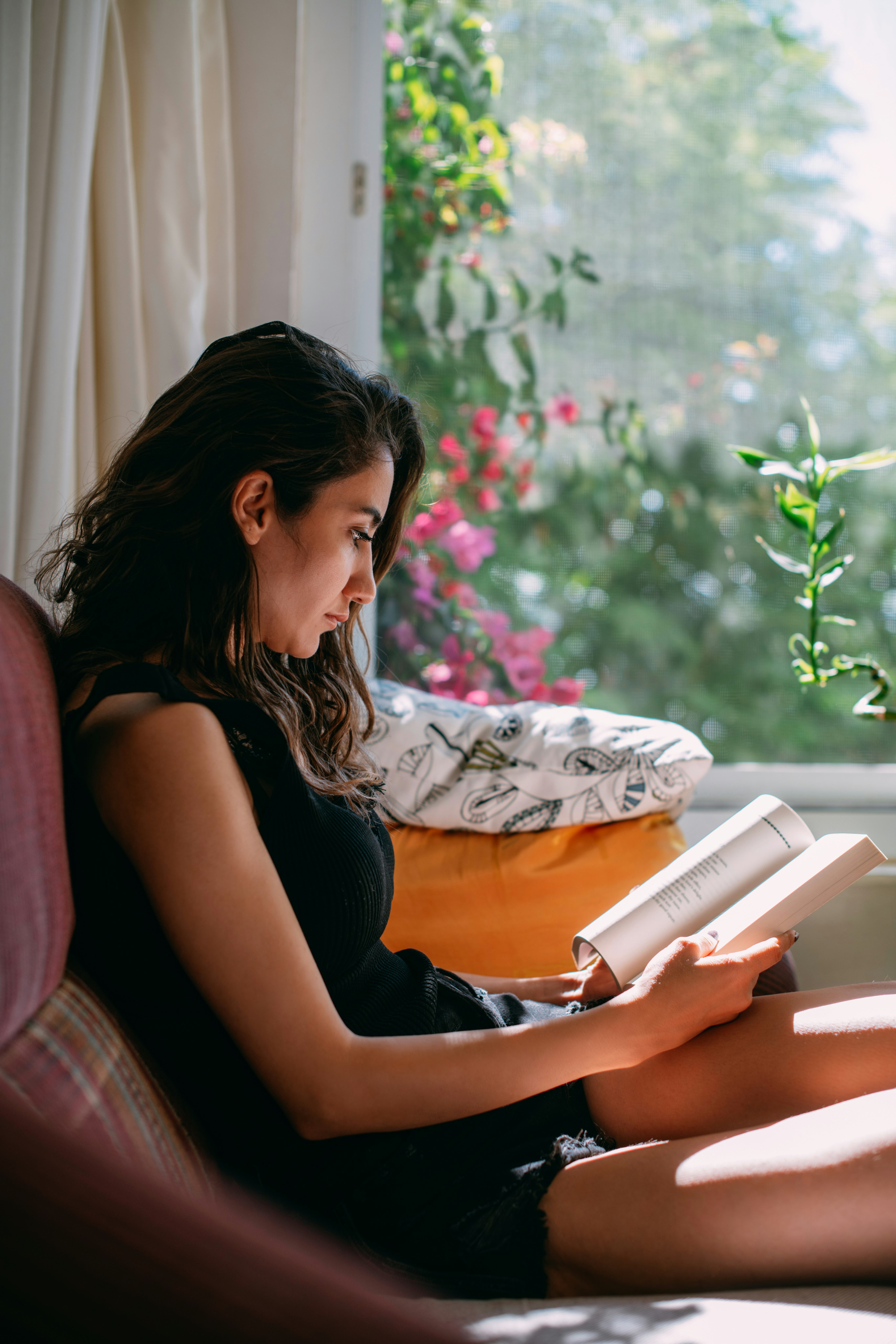 Young Woman Reading a Book by the Window at Home.