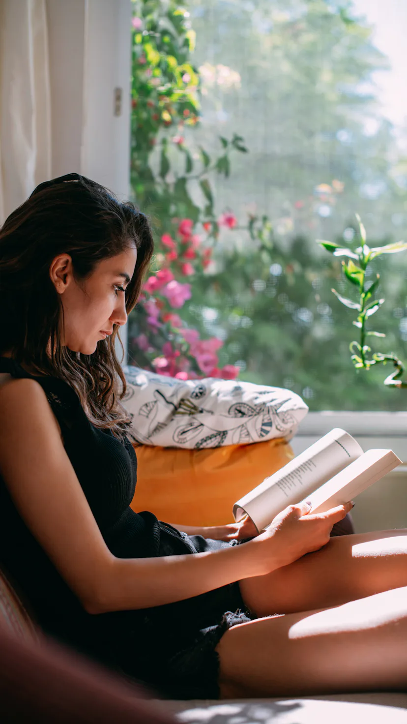 Young Woman Reading a Book by the Window at Home.