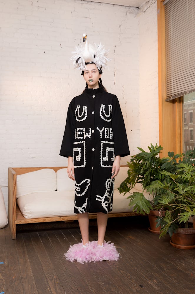 A model wearing a black shirt dress with white text saying "New York" and puffy pink slippers from D...