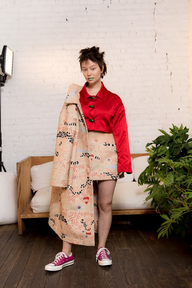 A model wearing a red shirt and holding a coat from Dauphinette's Fall 2022 collection.