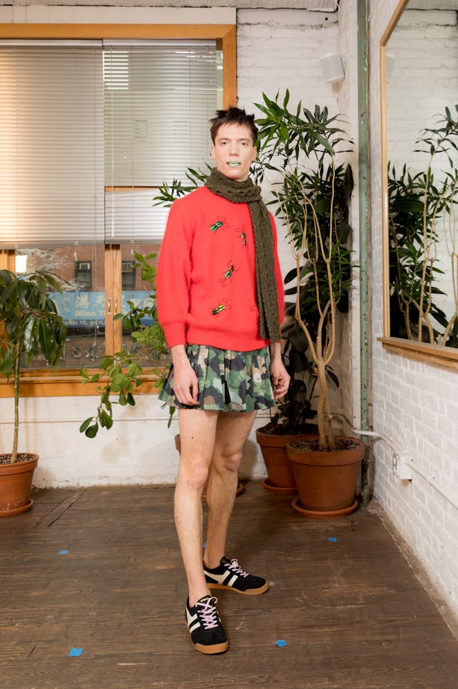 A model wearing a pink sweater,  camouflage skirt and black sneakers from Dauphinette's Fall 2022 co...