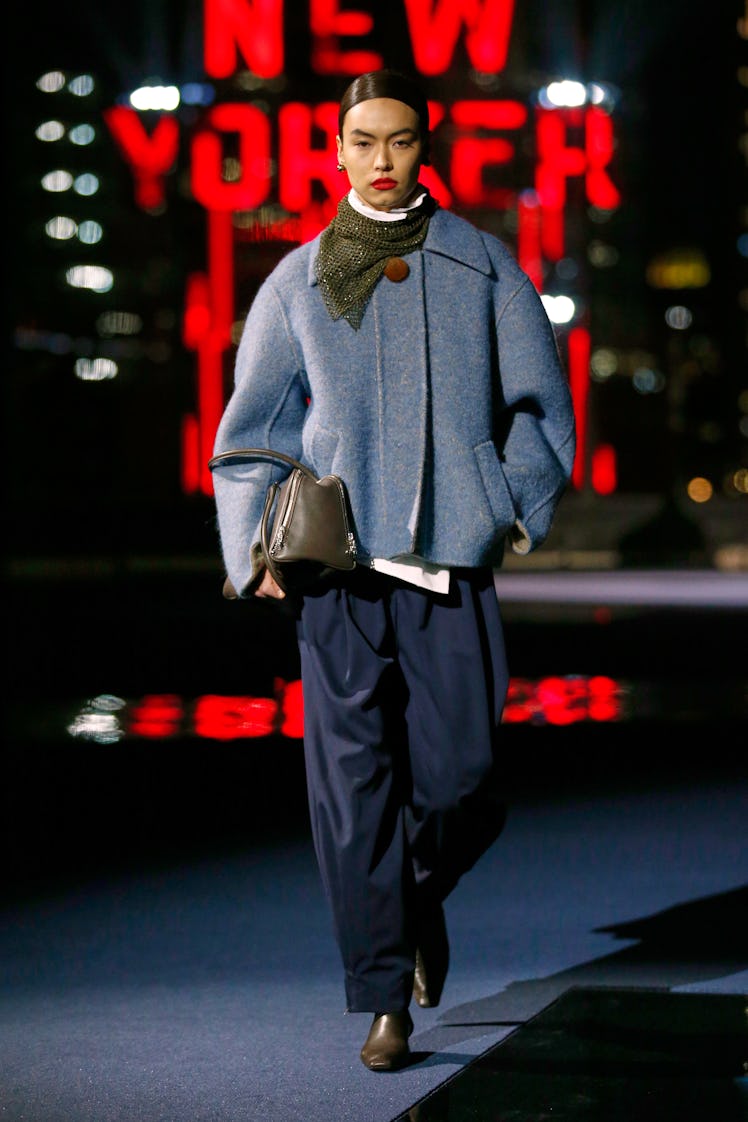 Model on the NY Fashion Week Fall 2022 runway in a Tory Burch blue coat, navy blue pants, and brown ...