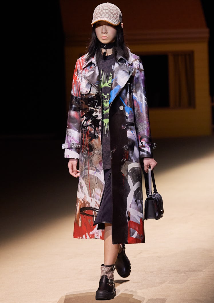 Model on the NY Fashion Week Fall 2022 runway in a Coach graffiti coat, white hat, carrying a black ...