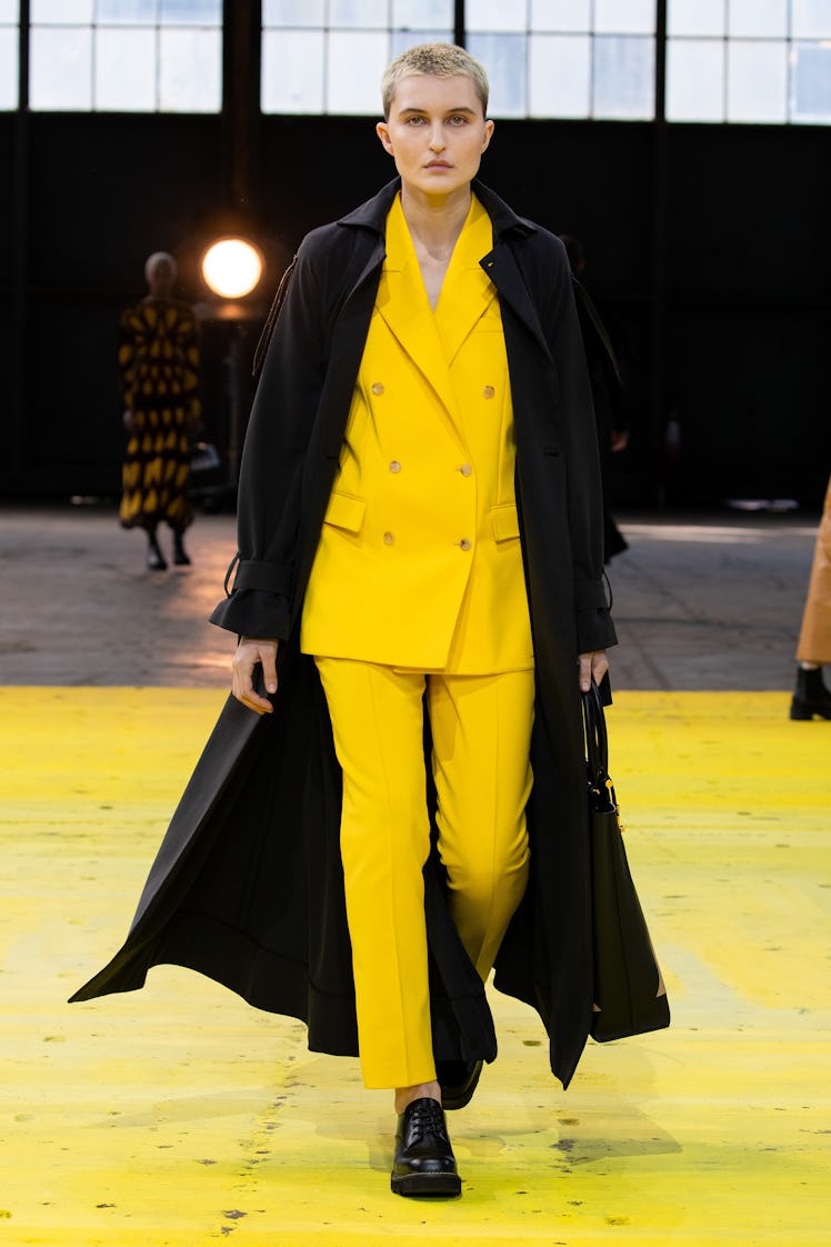 Model on the NY Fashion Week Fall 2022 runway in a Gabriela Hearst yellow suit with a long black coa...