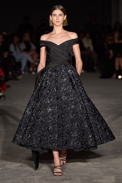 a model wearing a black full skirted A-line off-the-shoulder dress on the Christian Sirano runway