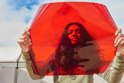 Young woman holding up red filter in front of face because she keeps seeing the same numbers (aka an...
