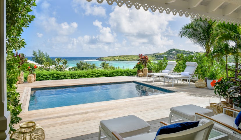 Rosewood Le Guanahani, a pool surrounded by a wooden floor, pool chairs and tropical trees