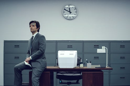Adam Scott as Mark Scout in the Apple TV+ series “Severance,”  sitting on the edge of a desk in a ba...