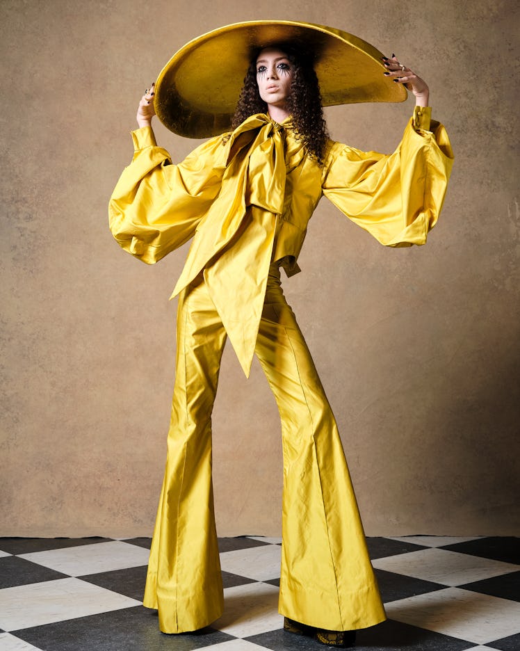 A model in a yellow blouse, trousers and oversized hat by Harris Reed