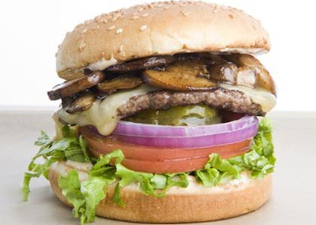 A portrait of a Rain City burger, piled high with lettuce, tomato, red onion, pickles, burger, melte...