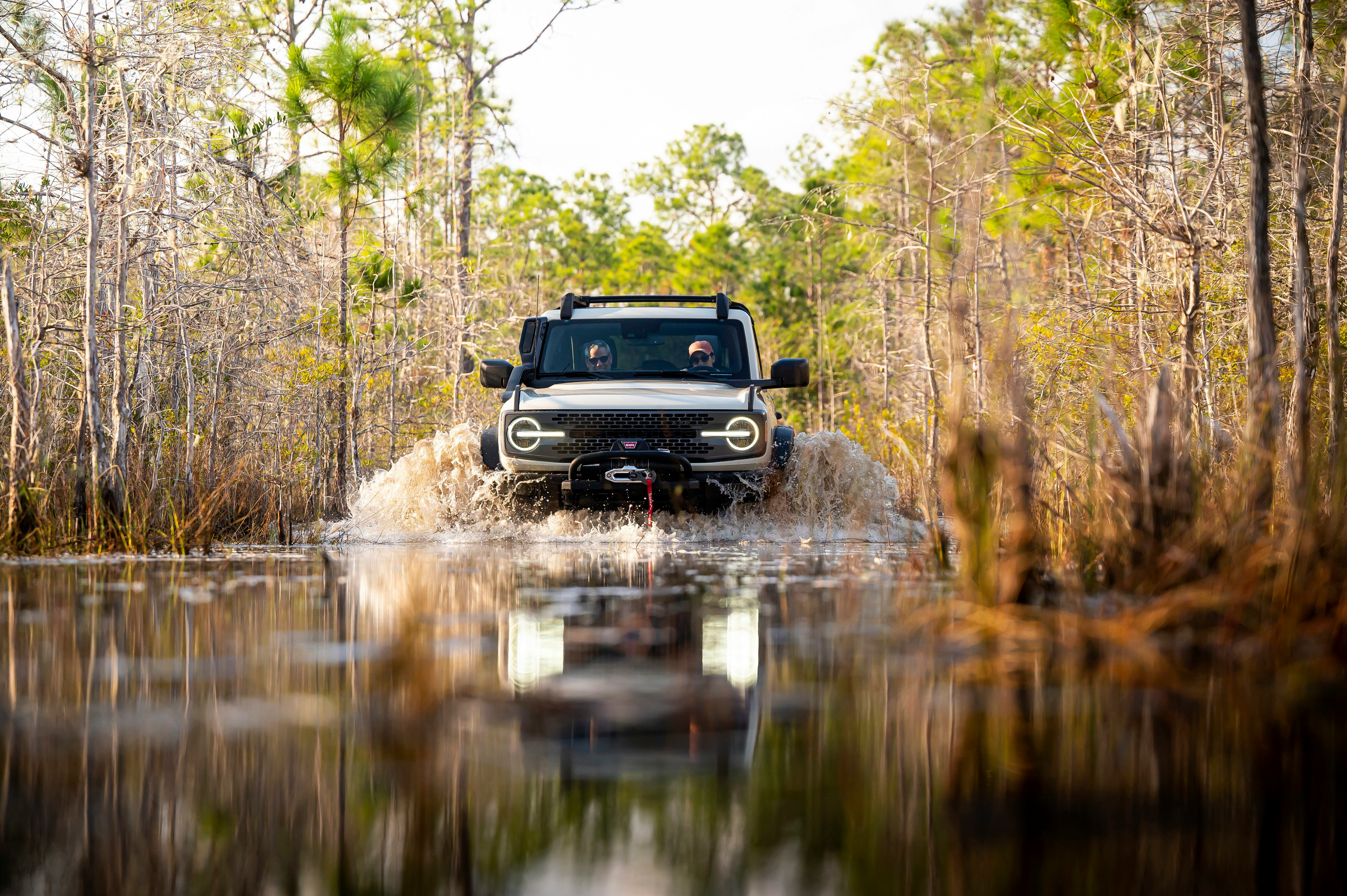 A grey-black Ford Bronco driving over a lake-like water surface