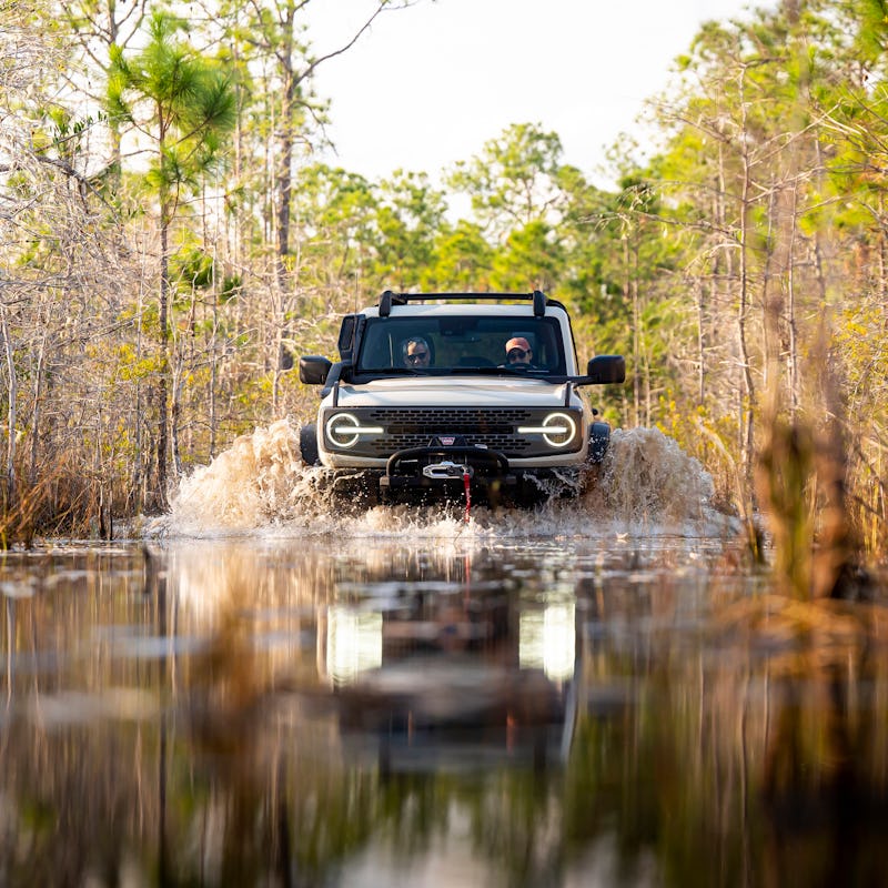A grey-black Ford Bronco driving over a lake-like water surface