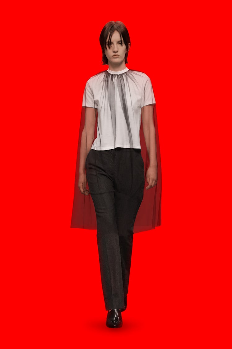 A model wearing a white shirt an black trousers and black tulle cape by Christopher Kane