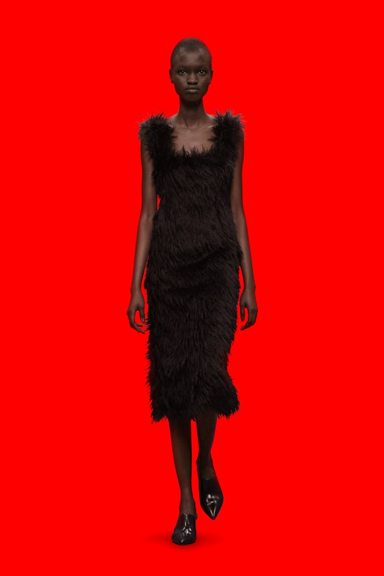A model wearing a black feather Christopher Kane dress with a red background