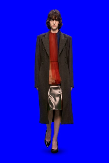 Model in gray coat, sheer red top and shiny skirt