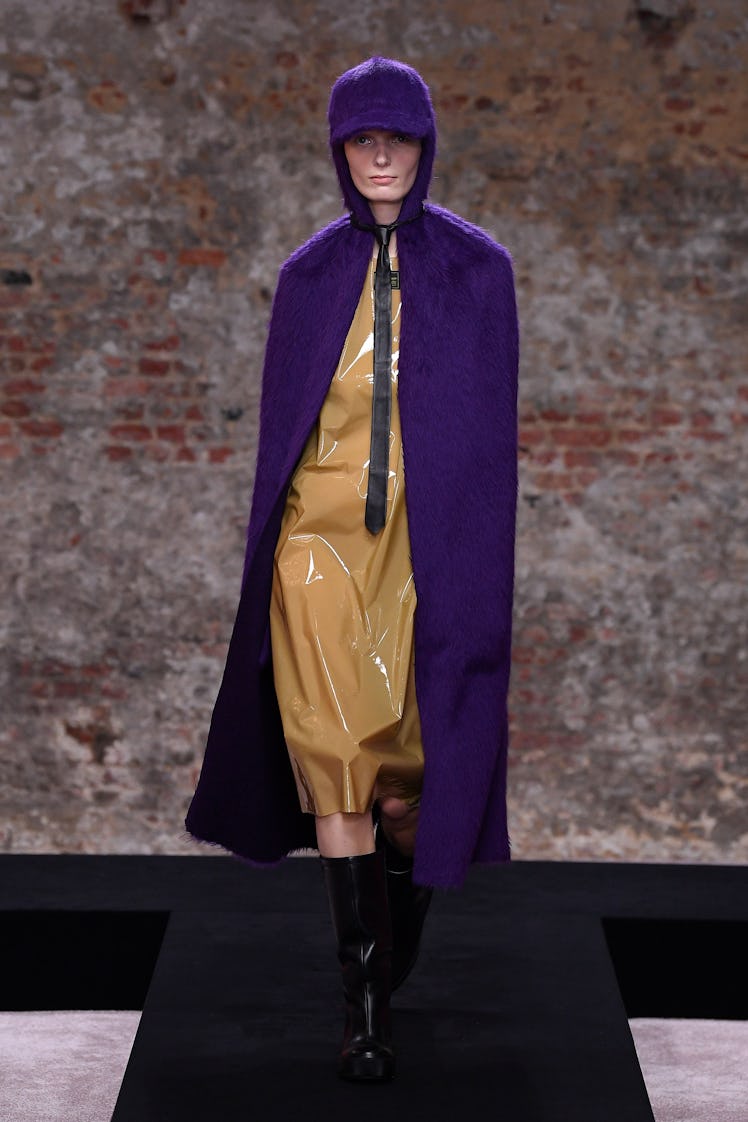 A model wearing a yellow dress and purple cape with hat by Raf Simons at the London Fashion Week Fal...