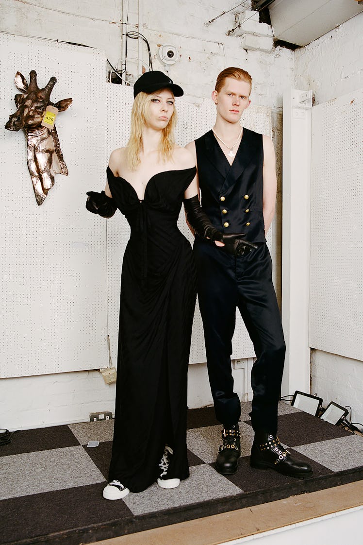 A model in a black dress and cap and a model in a black waistcoat and trousers by Vivienne Westwood