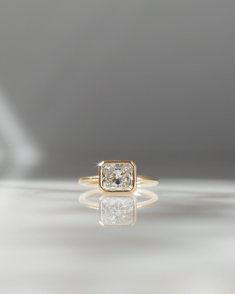 a bezel-set radiant-cut diamond engagement ring in yellow gold by Grace Lee
